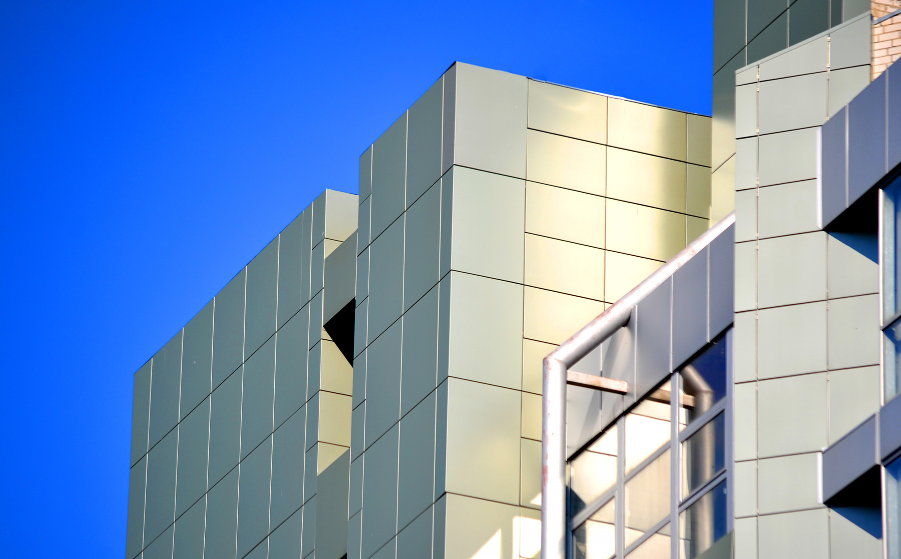 Saubere Aluminiumfassade eines modernen Gebäudes, die im Sonnenlicht glänzt, mit einem klaren blauen Himmel im Hintergrund nach einer Aluminiumfassadenreinigung.