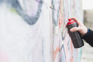 Hand hält eine Sprühdose und sprüht Graffiti auf eine bunte Wand.