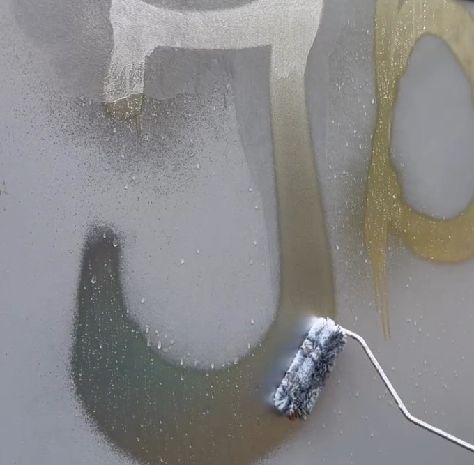 Auftragen eines Graffitientferners mit Farbrolle auf beschmierte Wand.