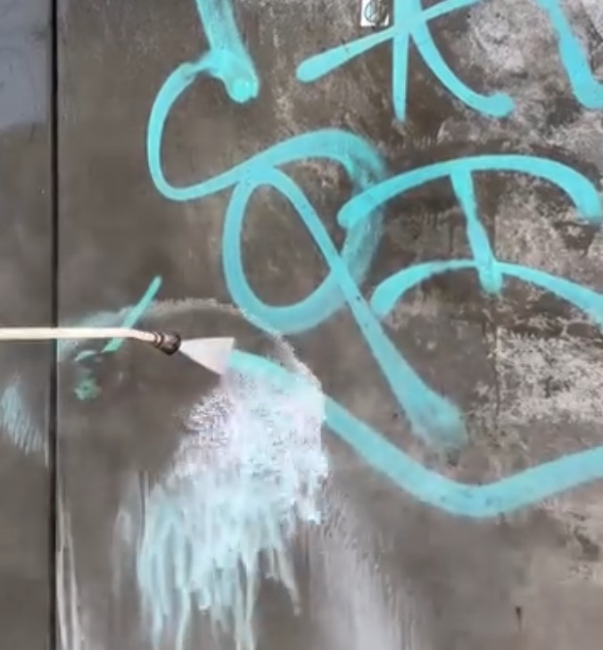 Wasserstrahl entfernt türkisfarbenes Graffiti von glatter Betonwand