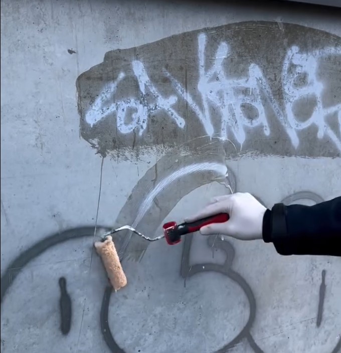 Auftrag eines Reinigungsmittels auf Graffiti auf Betonwand per Farbroller