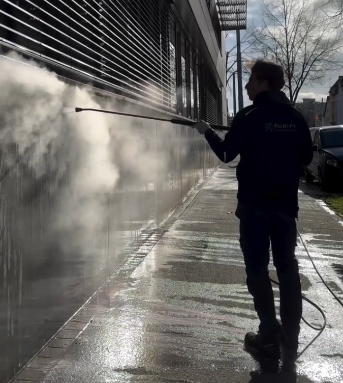 Purify-Mitarbeiter entfernt Graffiti mit Niederdruckreiniger von moderner Fassadenfläche.