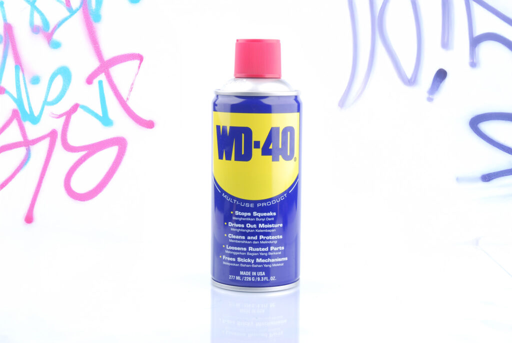 WD-40 Spraydose vor einer mit buntem Graffiti besprühten Wand.