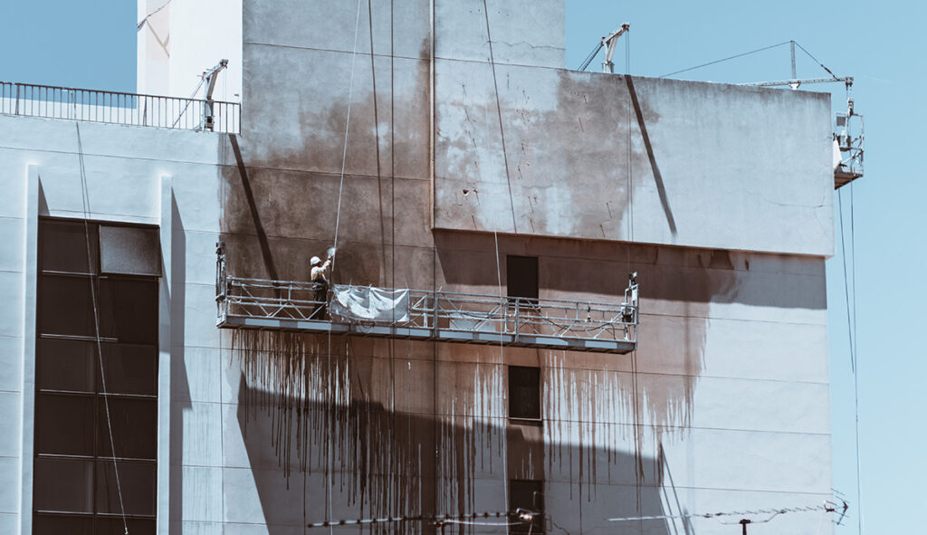 Arbeiter reinigt stark verrußte Fassade nach einem Gebäudebrand mit Spezialtechnik.
