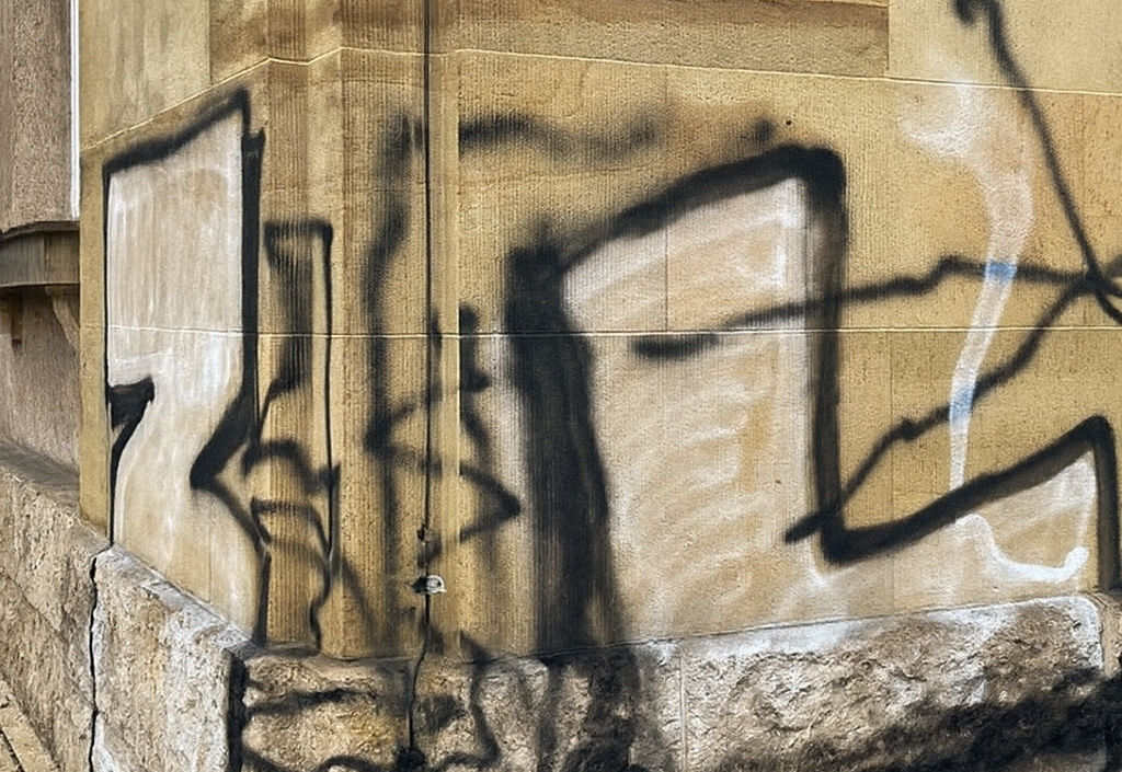 Graffiti auf hellbrauner Natursteinfassade mit schwarzer und weißer Sprühfarbe.