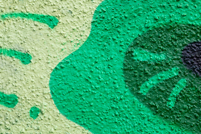 Grünes Graffiti auf strukturierter Putzfassade aus der Nähe.