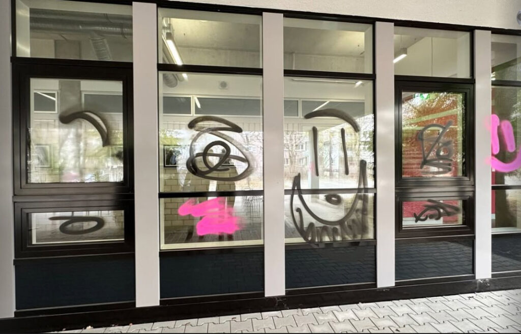 Fensterfront mit Graffiti in Schwarz und Pink – Beispiel für verschmierte Glasfassade vor der Reinigung.