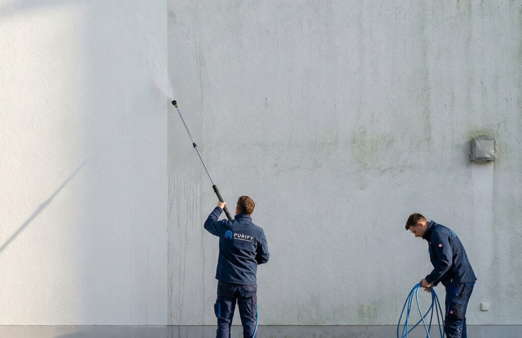 fassadenreinigung-niederdrucktechnik-putzfassade-purify Zwei Fachkräfte reinigen eine Putzfassade mit Niederdrucktechnik und Teleskoplanze bei der professionellen Fassadenreinigung.