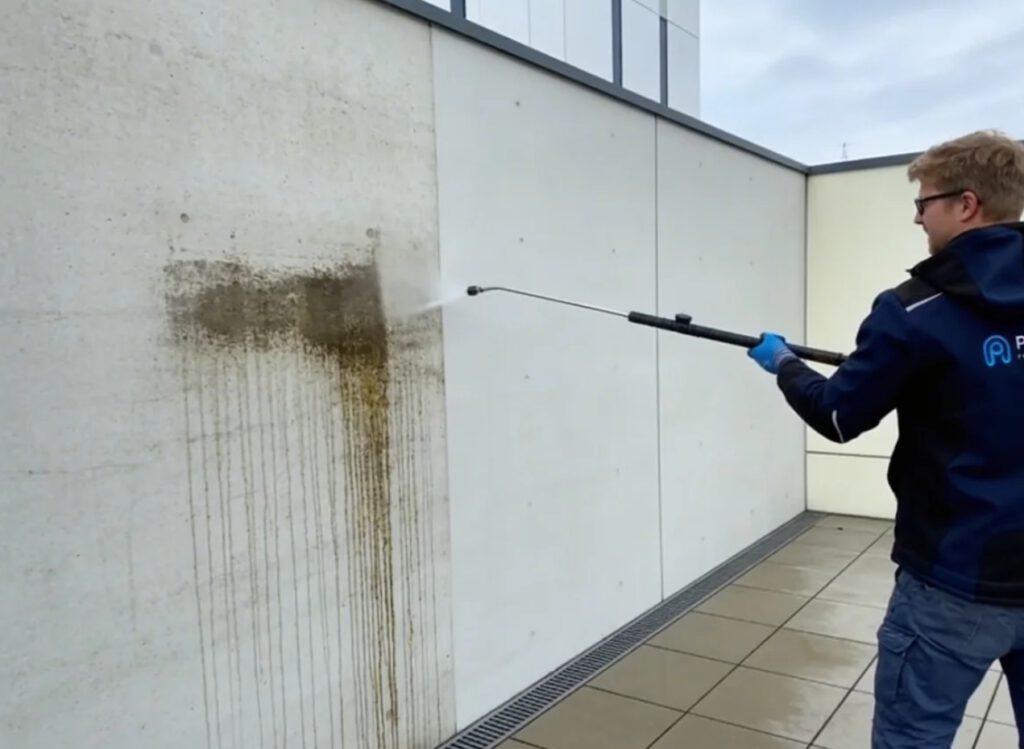 Fettflecken auf Beton entfernen mit Niederdrucktechnik Techniker entfernt Fettflecken auf Beton mit schonender Niederdrucktechnik an einer Betonwand
