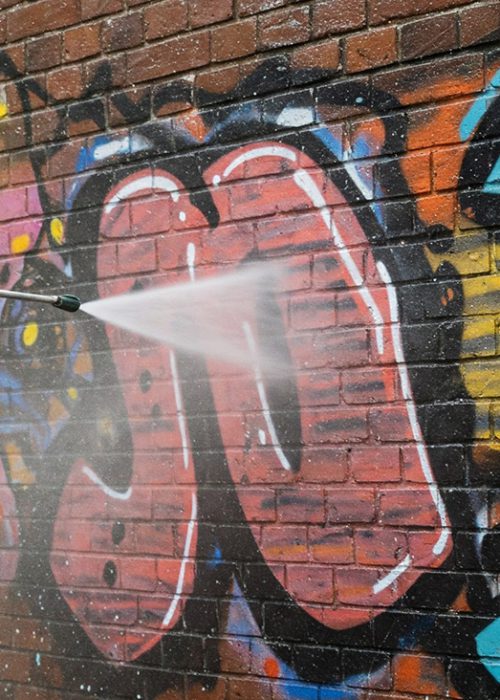 Ein Wasserstrahl entfernt Graffiti von einer roten Klinkerfassade in Esslingen – professionelle Fassadenreinigung mit schonender Niederdrucktechnik.