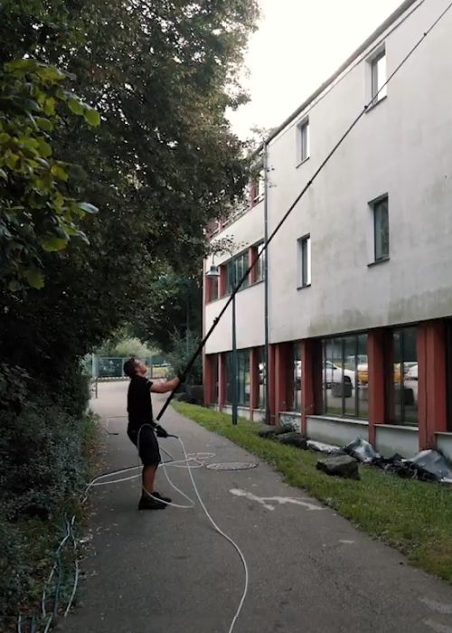 Ein Mitarbeiter reinigt mit einer extra langen Teleskoplanze die stark verschmutzte Fassade eines mehrstöckigen Gebäudes in Reutlingen – Fassadenreinigung mit dem Purify-Niederdrucksystem.
