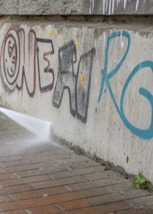 Graffiti wird im Sockelbereich einer Betonfassade in Freiburg mit Wasserstrahl entfernt.
