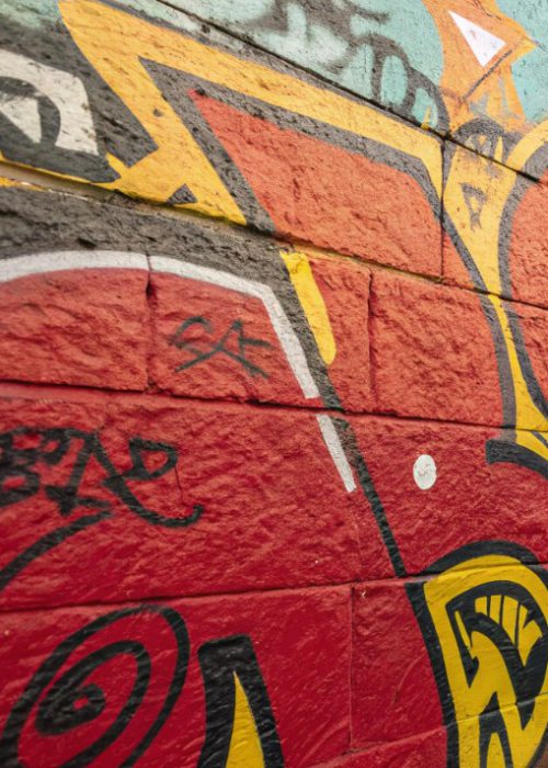 Nahaufnahme einer rot besprühten Backsteinmauer mit auffälligem Graffiti